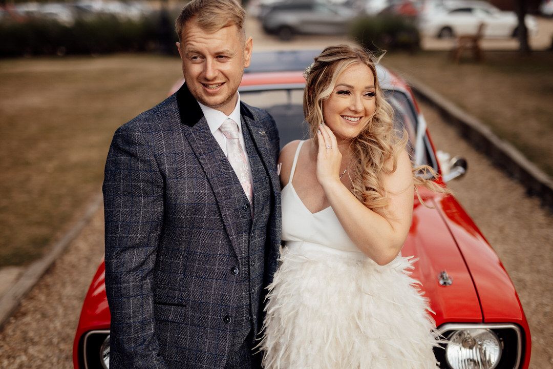 Classic red vintage car serves as backdrop for elegant wedding portraits.