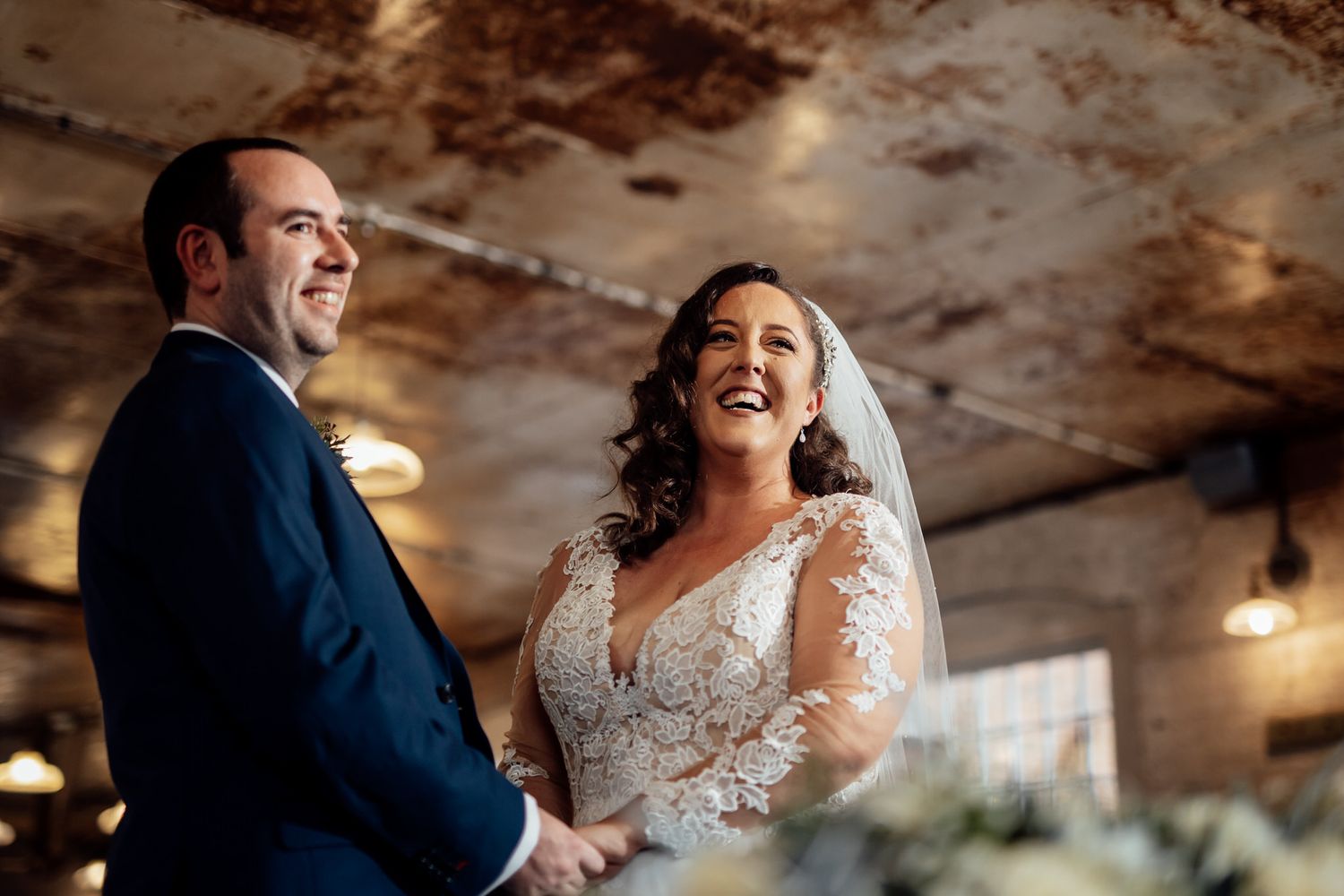 Candid wedding moments captured in rustic venue with natural light and exposed ceiling.
