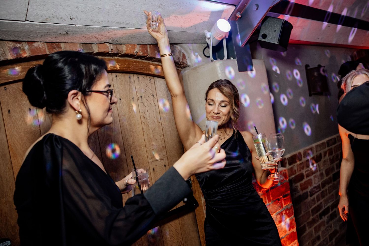 Wedding party dancing and celebrating on a rustic wooden dance floor with atmospheric lighting.