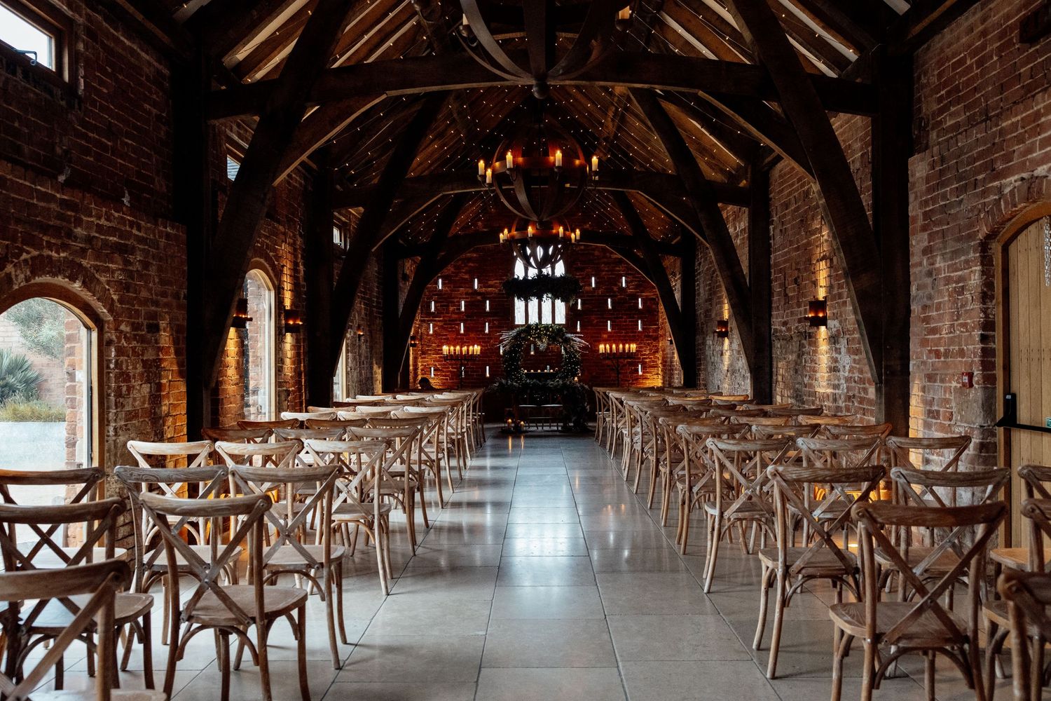 Rustic barn wedding venue with exposed wooden beams, brick walls and crossback chairs lined up for ceremony.