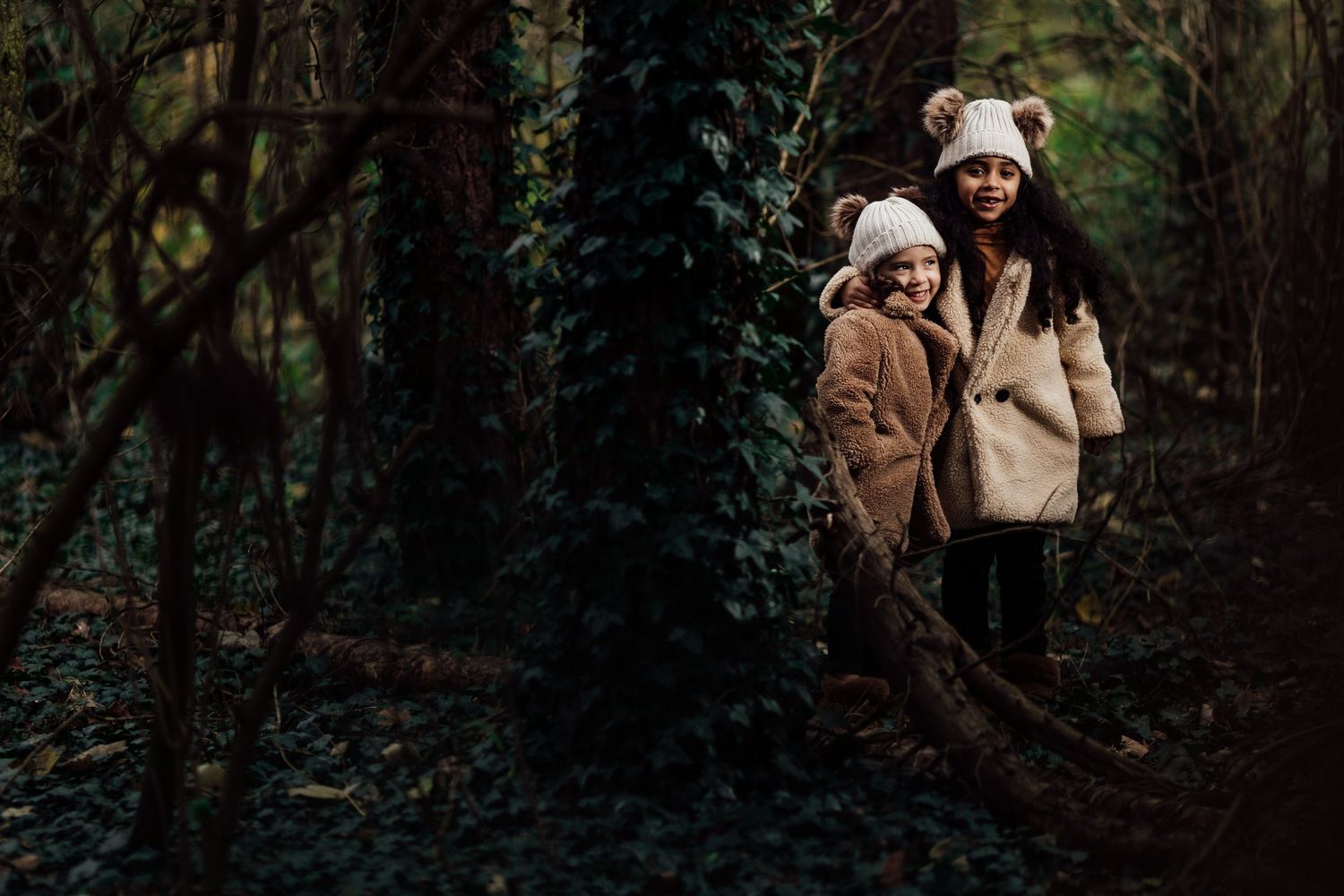People in warm winter clothing share an intimate moment in a dark wooded setting.