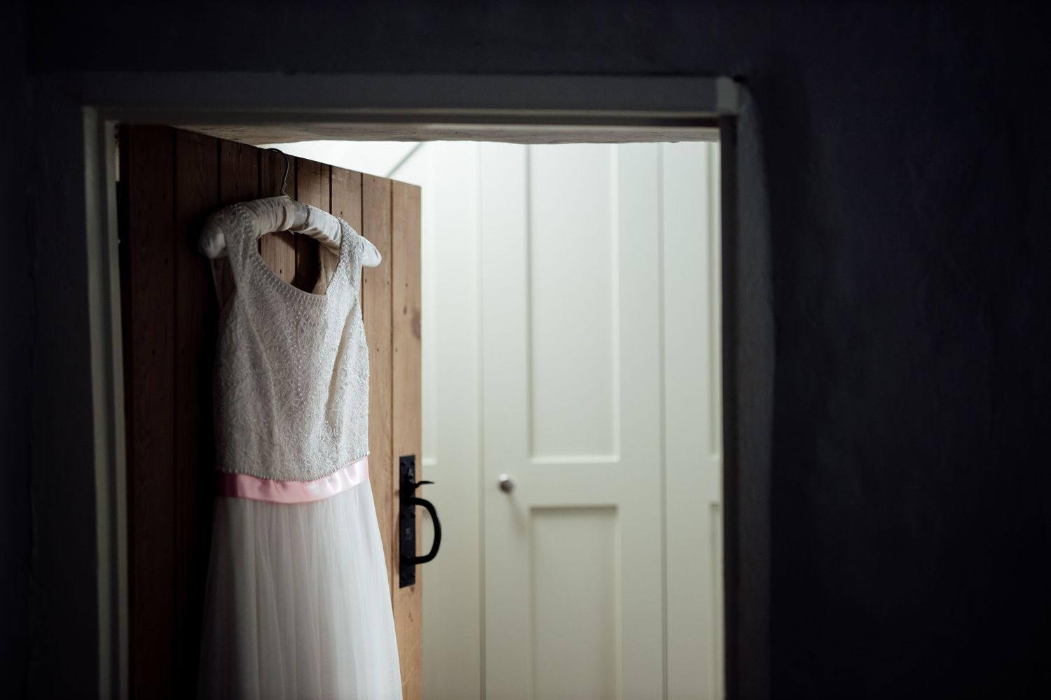 White wedding dress hanging in doorway with natural light streaming in.