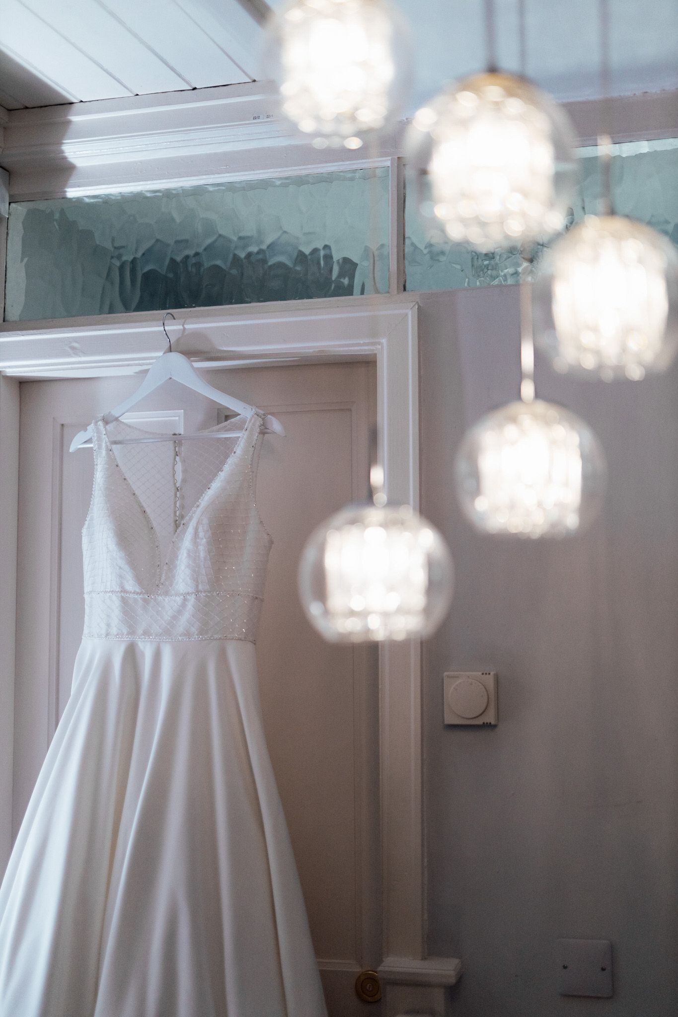 White wedding dress hanging from ceiling with crystal chandeliers in an elegant dressing room.