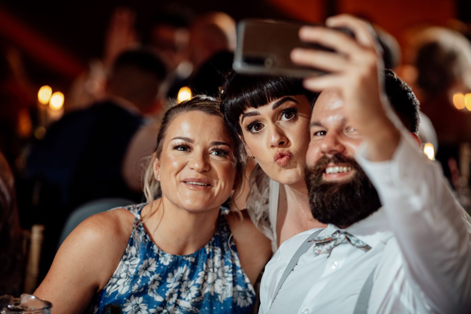 Wedding party guests taking selfies and dancing during an indoor reception celebration.