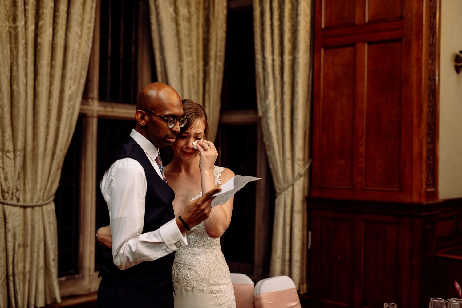 Intimate wedding reception moment captured in warm indoor lighting with elegant curtains.