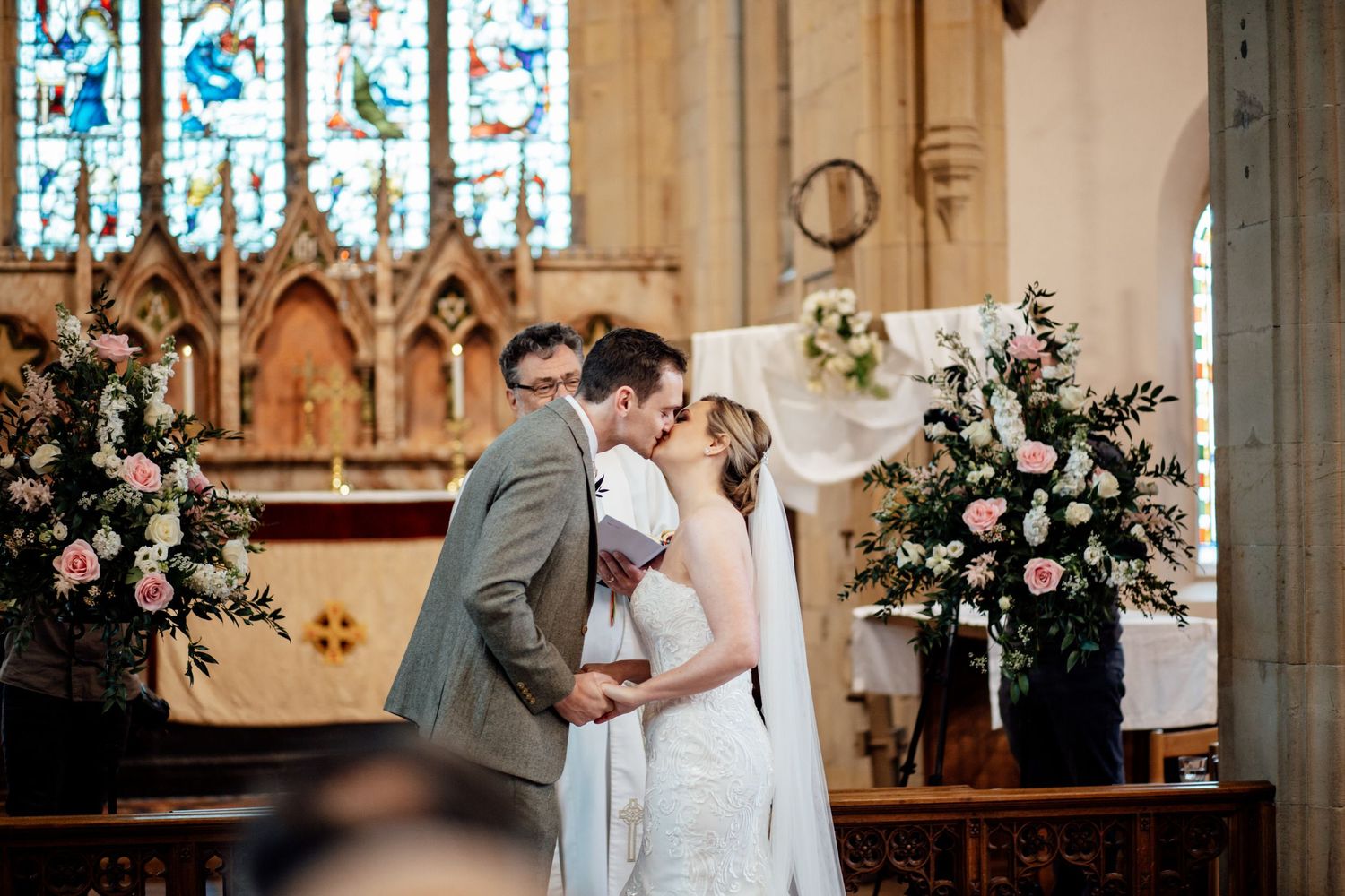 Wedding ceremony in a beautiful church with stained glass windows and floral arrangements.