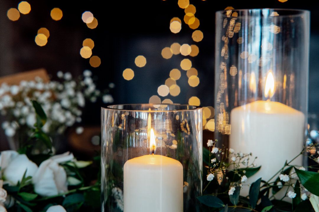 Elegant wedding reception decor with glowing candles in glass holders and bokeh lights.