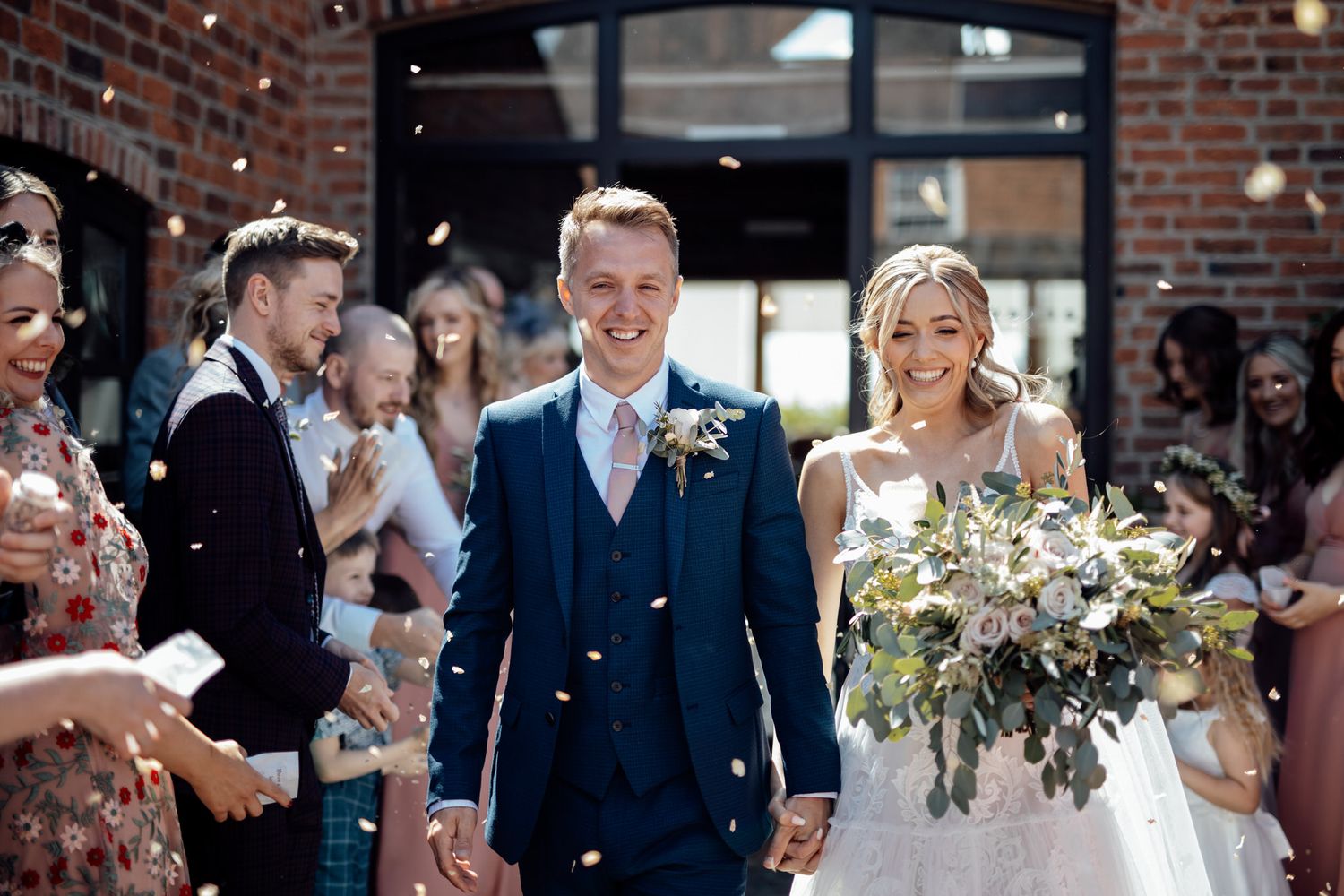 Festive outdoor wedding scene with confetti and brick building backdrop.