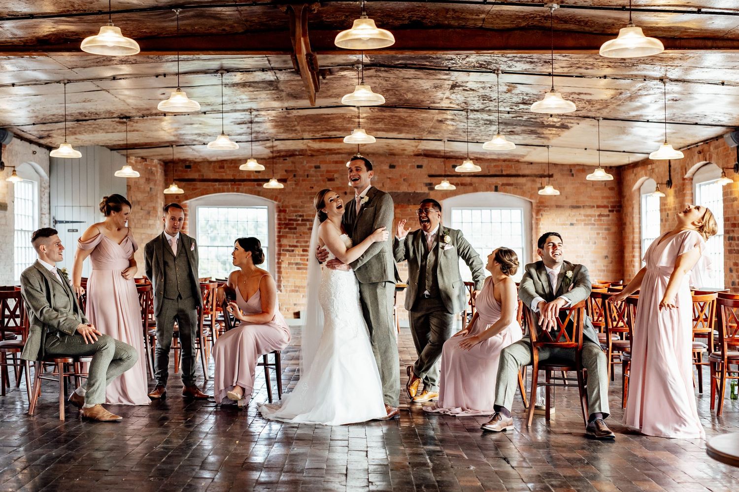 Wedding party stands in rustic venue with wooden ceiling and pendant lights.