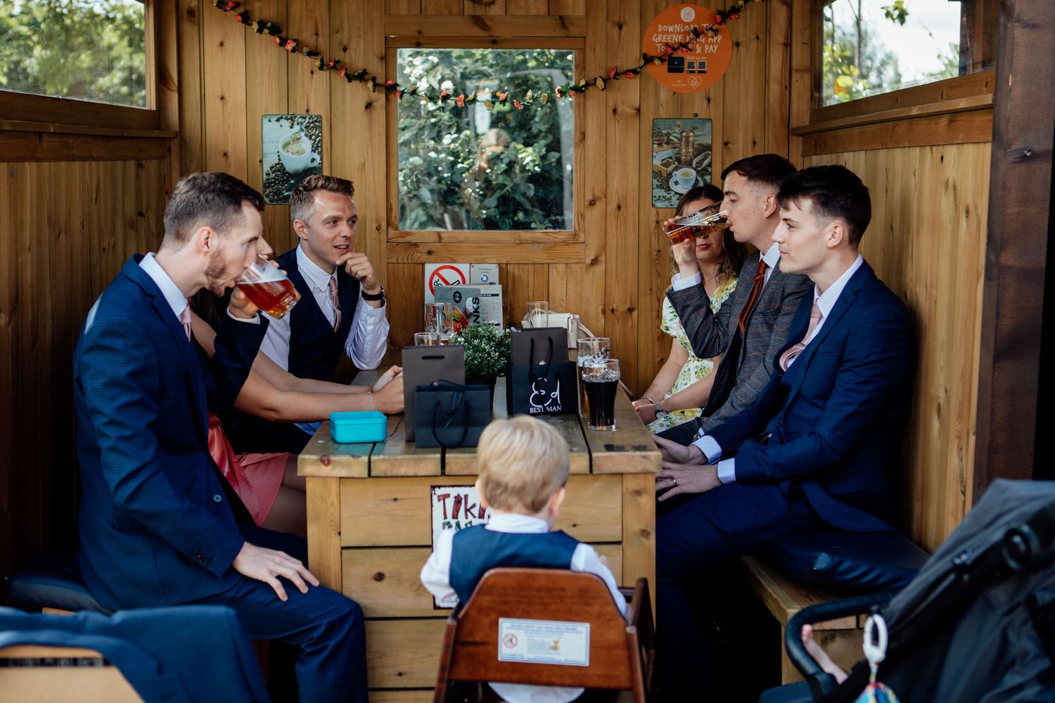 Wedding party enjoying drinks and conversation in a rustic wooden venue setting.