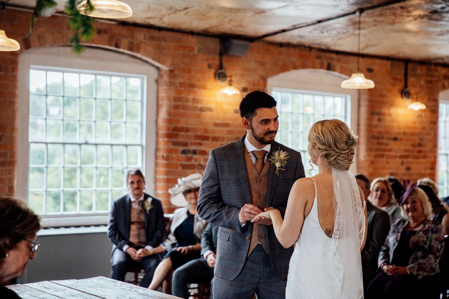 Guests mingle during a wedding reception in a rustic brick-walled venue with natural lighting.