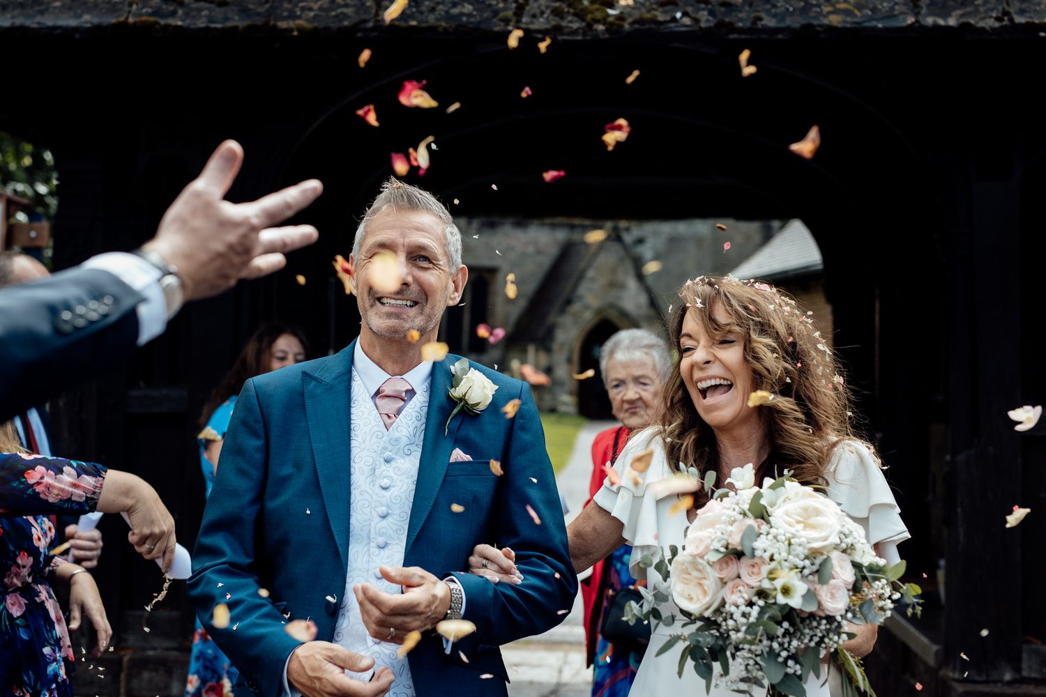 Wedding couple exits venue as guests throw flower petals in celebration.