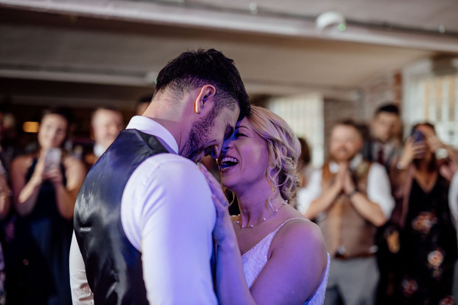 A couple shares their first dance at a wedding reception with guests watching in the background.