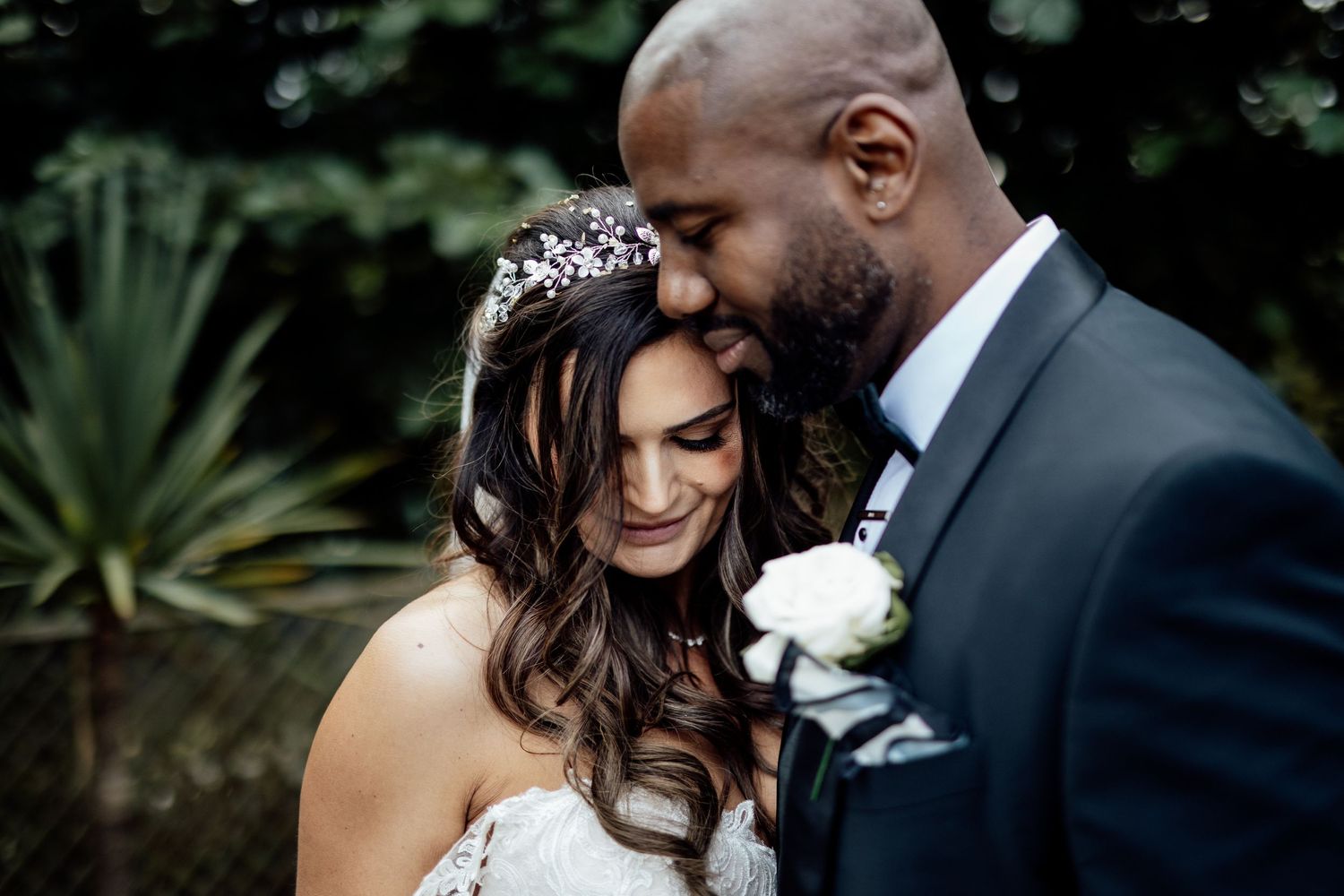 A tender moment between newlyweds in a garden setting with a sparkling tiara and white boutonniere.