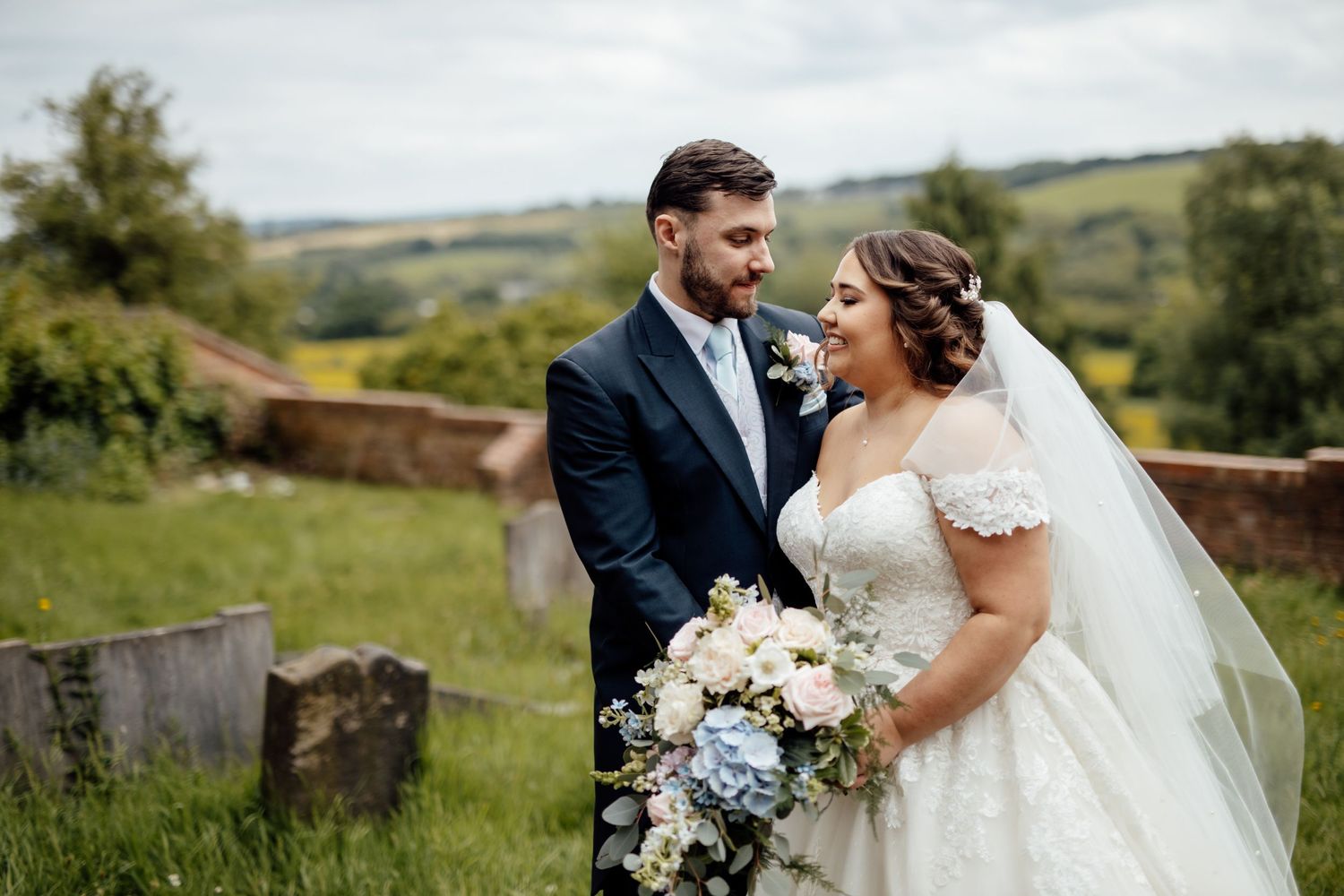 Wedding couple shares intimate moment in countryside setting with rolling hills in background.
