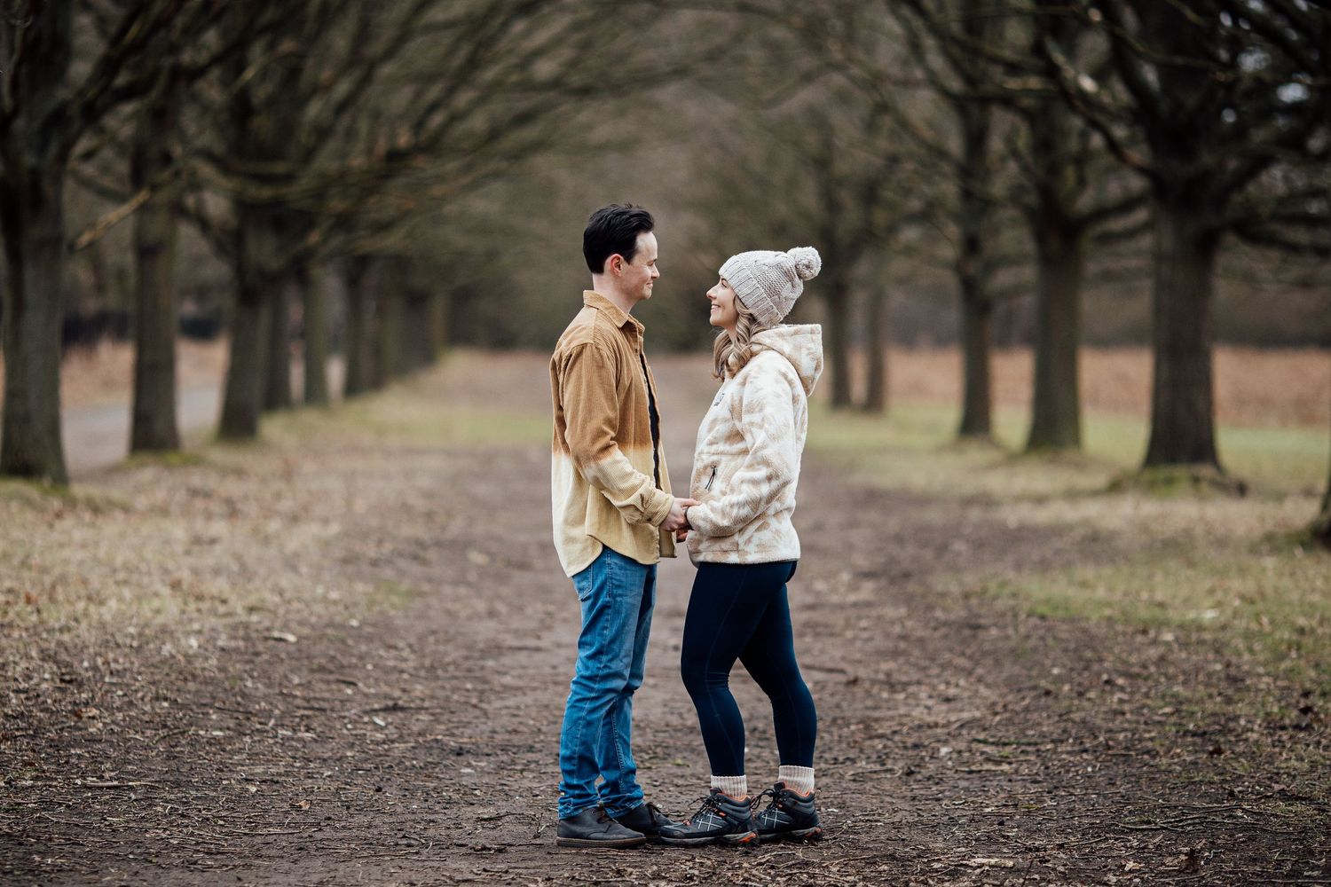 Couple walking hand in hand through a park with bare winter trees in the background.