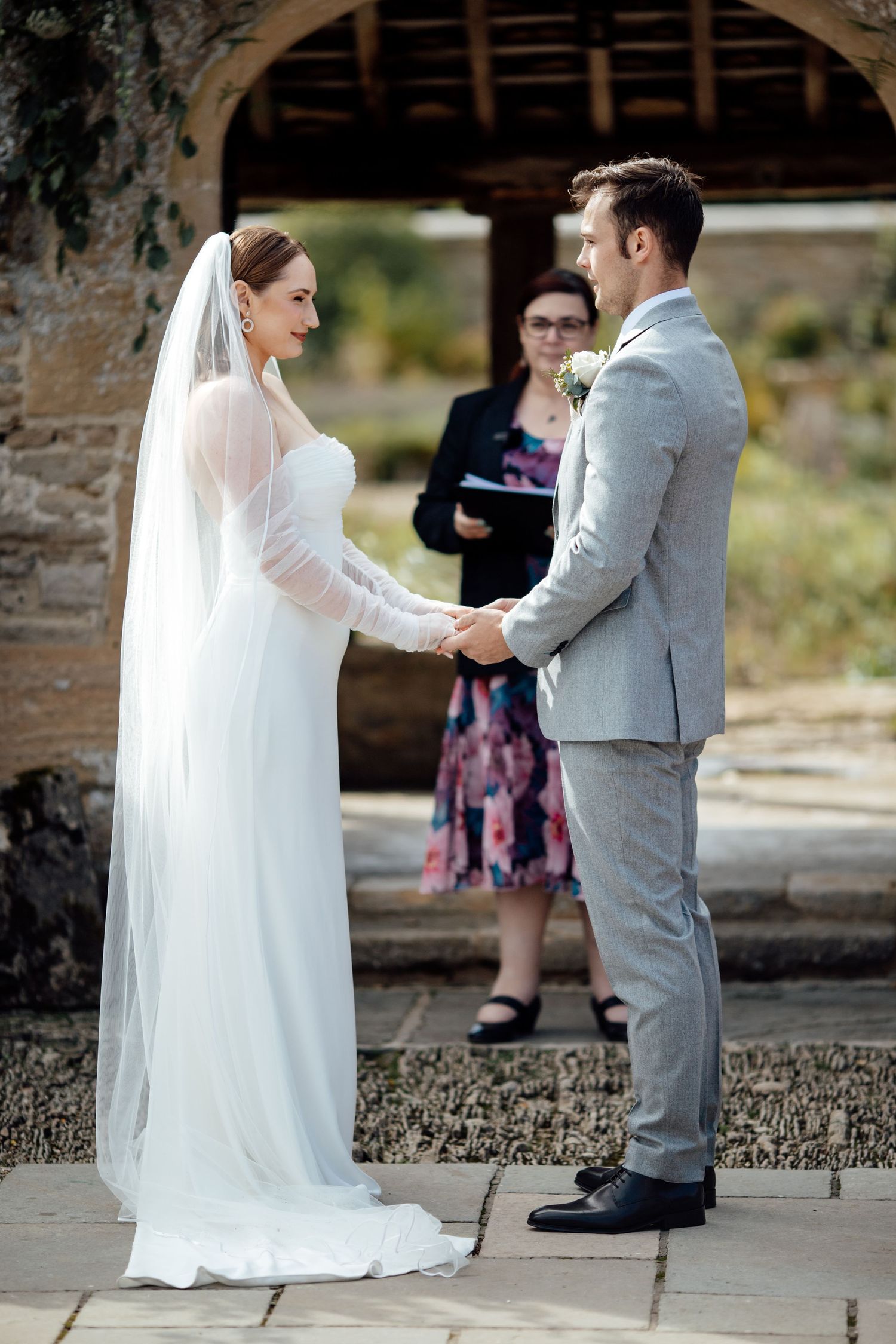 Wedding ceremony taking place under a stone archway with natural lighting.