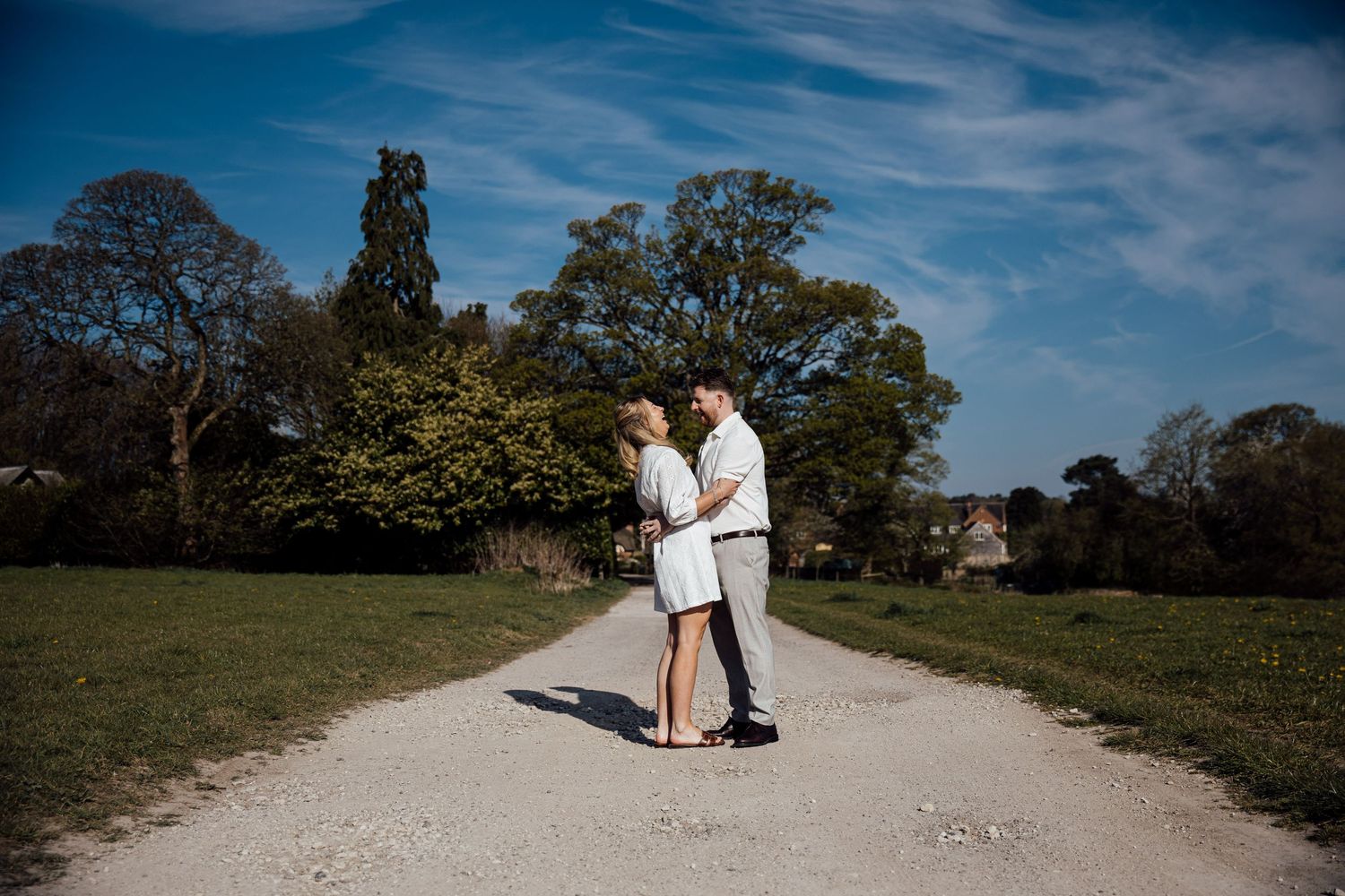 A couple enjoys a romantic walk along a winding gravel path under blue skies.