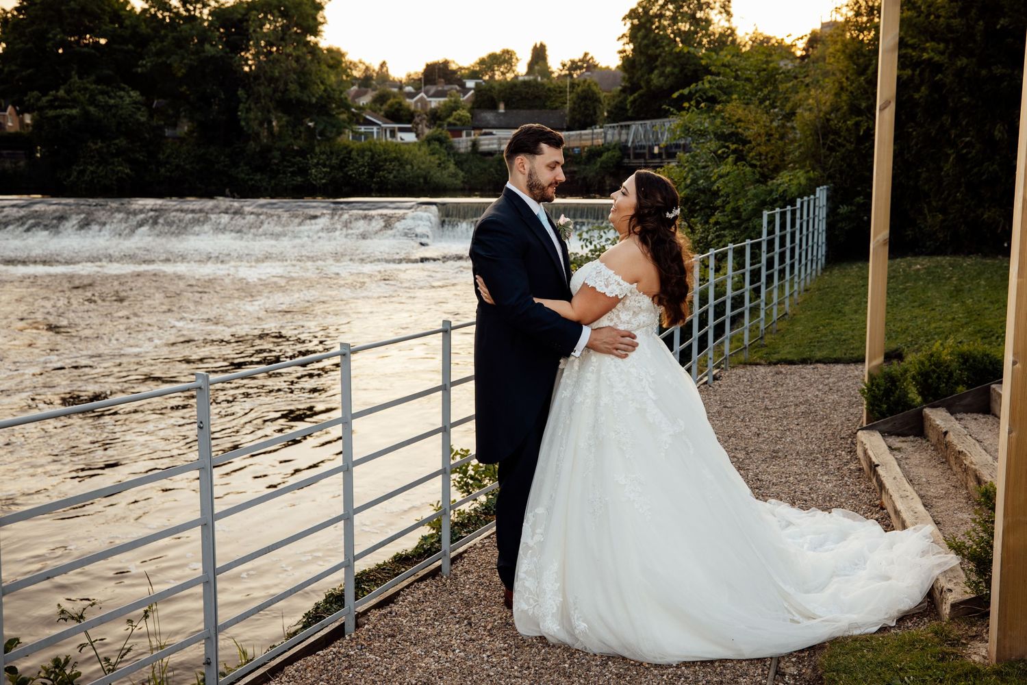 Romantic sunset wedding photos of a couple posing along a waterfront railing.