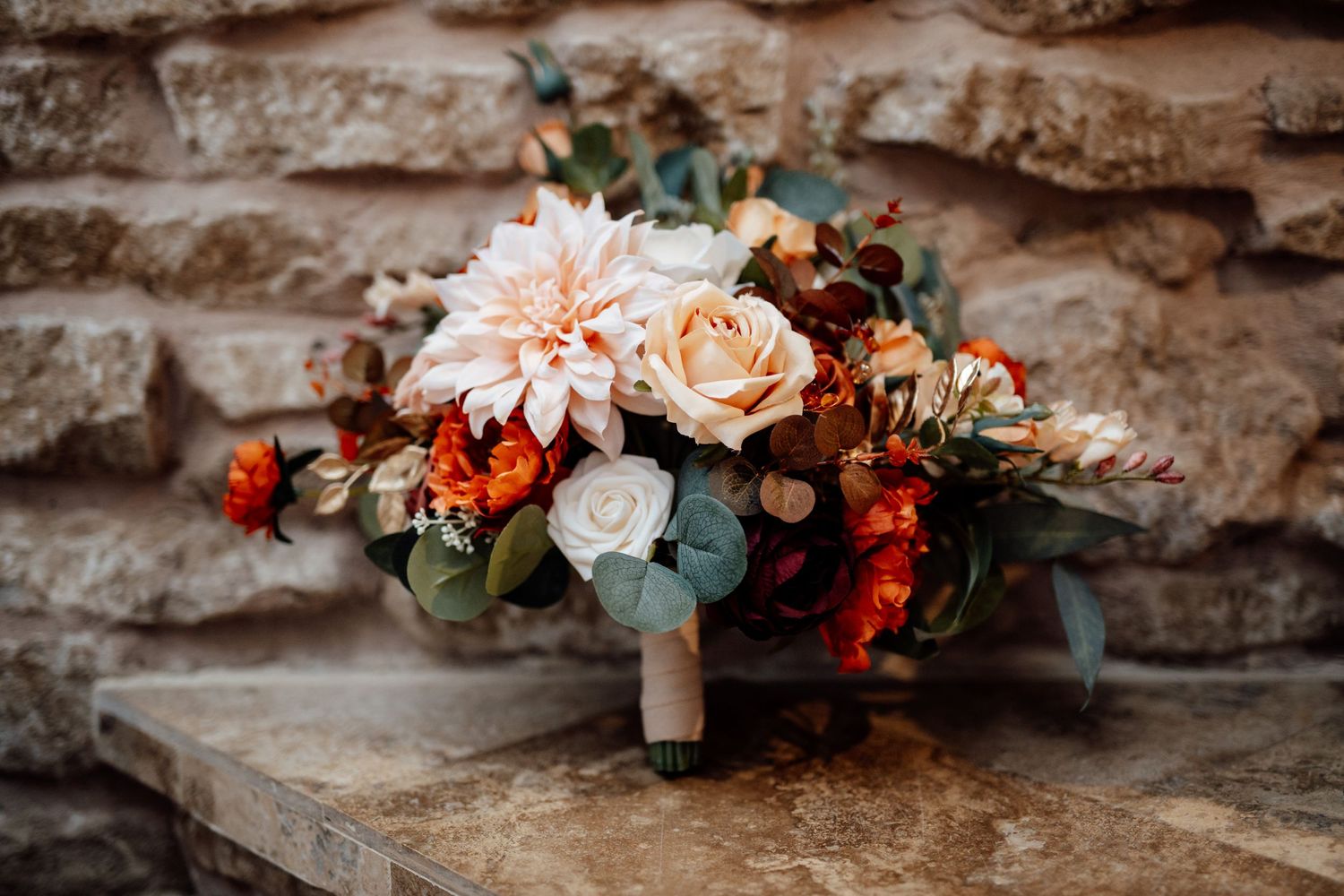 Romantic floral arrangements with peach roses and greenery displayed on stone ledge.