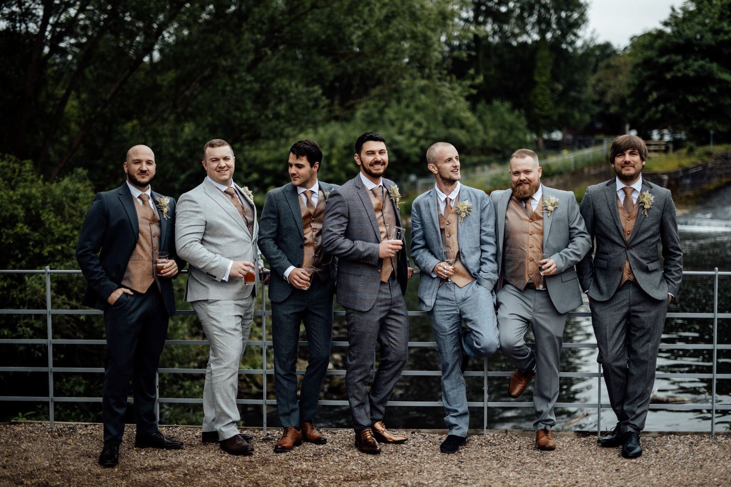 Wedding party members sitting casually on outdoor railing for group photo.