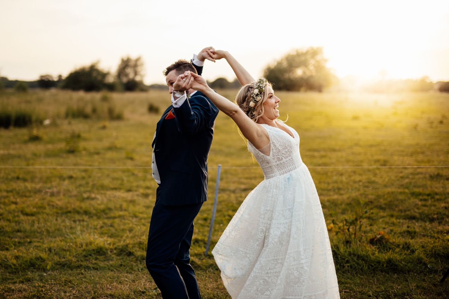 A couple makes heart shapes with their hands against a golden sunset in a field.