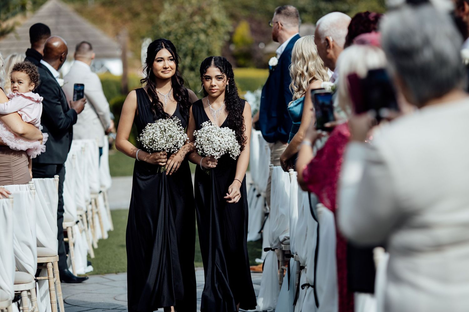 Wedding ceremony guests seated in rows with bridesmaids in black dresses.