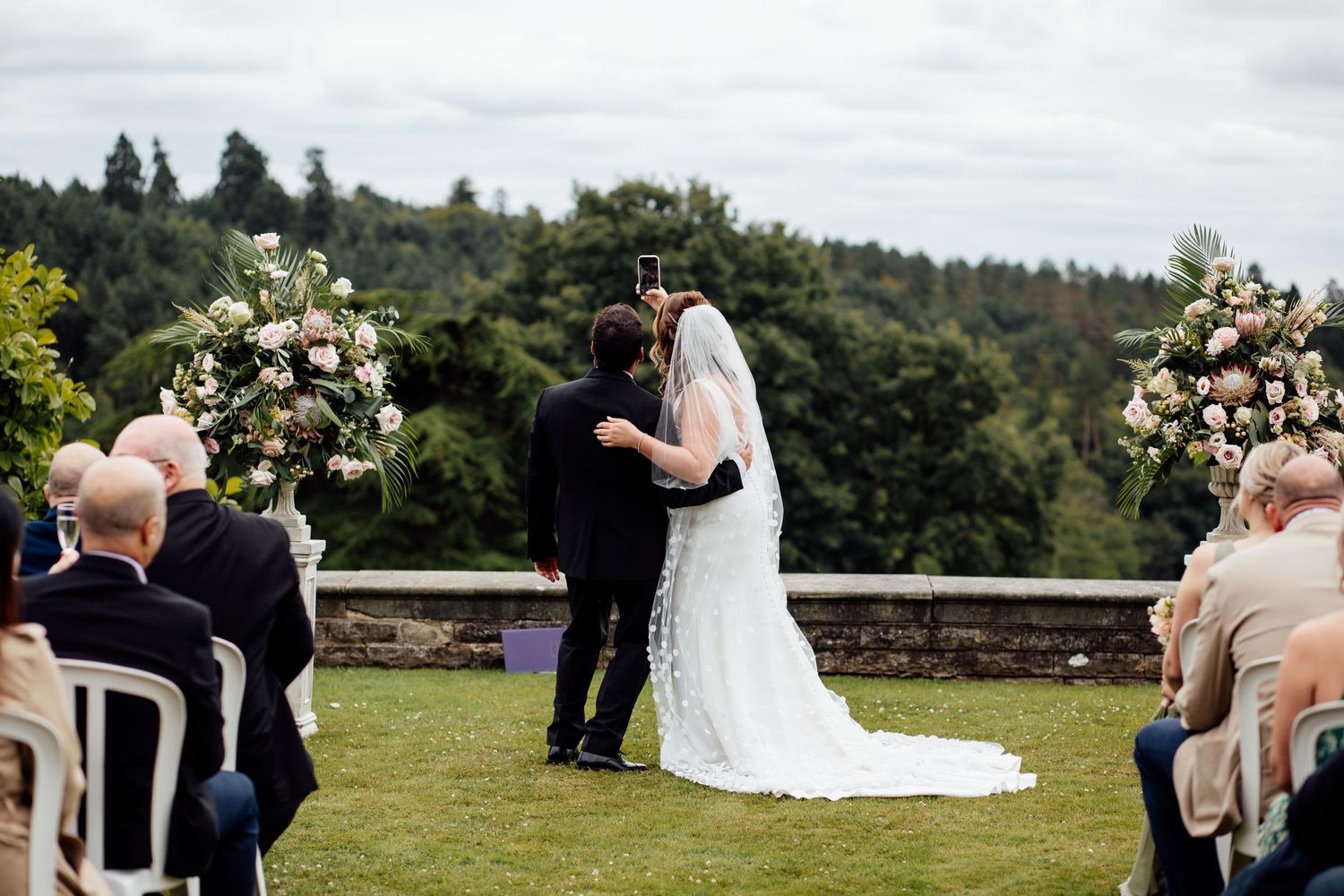 Wedding party and guests gathered on a scenic hilltop venue during ceremony.
