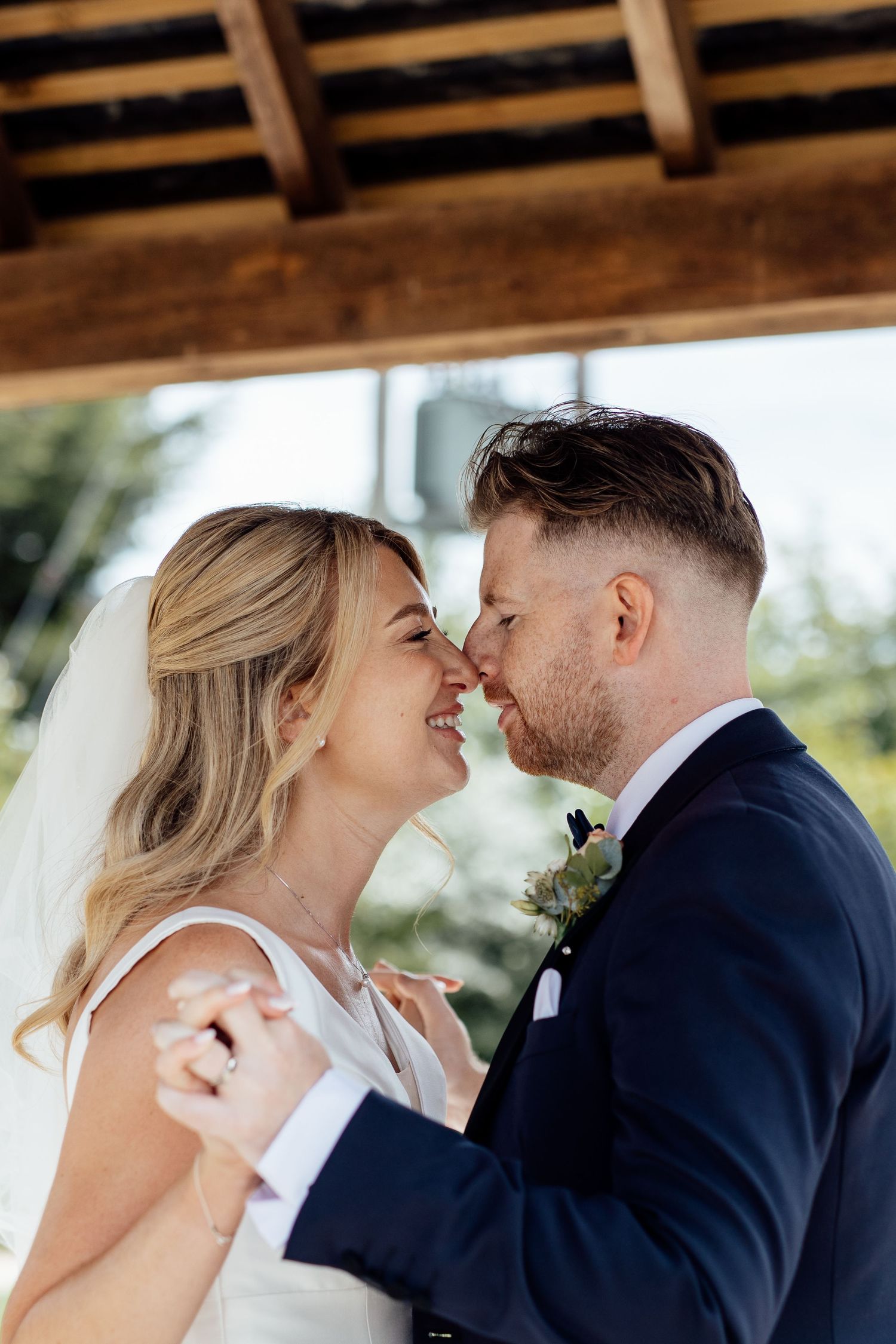 Romantic wedding couple shares intimate moments under wooden beams.