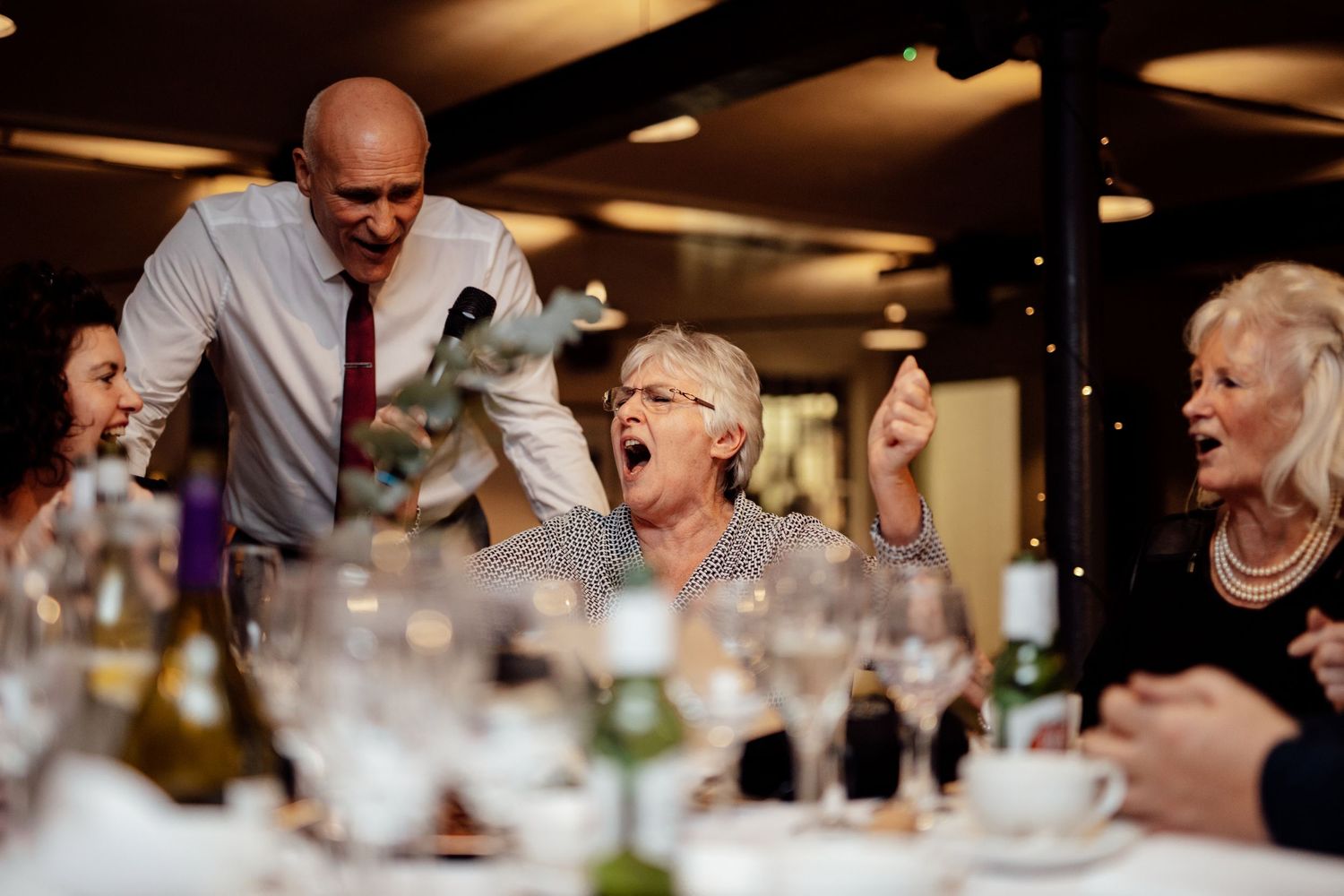 Wedding reception dinner scene with warm lighting and animated conversation among guests.