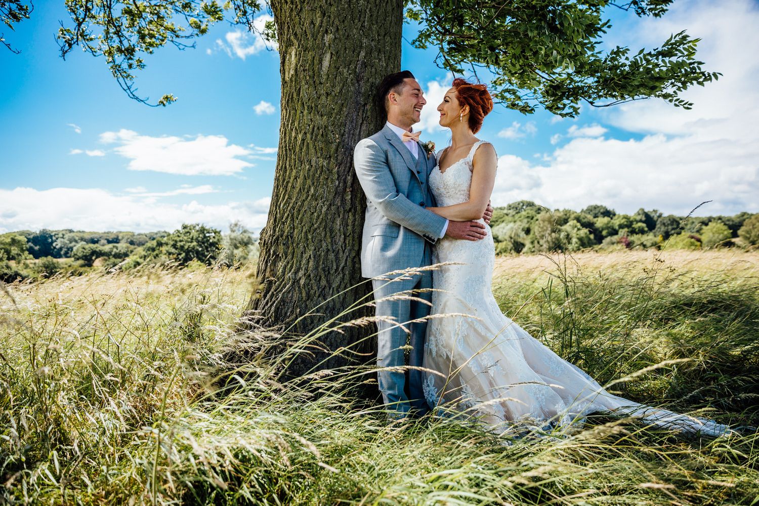 A romantic wedding portrait under a large oak tree in a summer meadow.