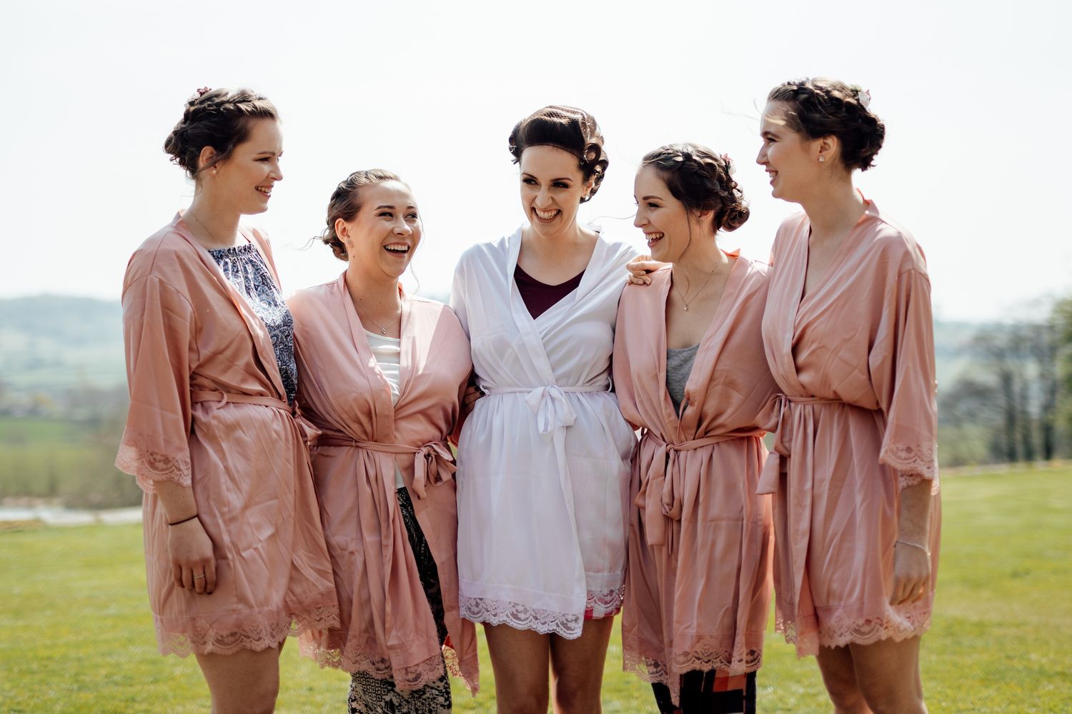 Group wearing blush pink robes standing together in a sunny outdoor setting.