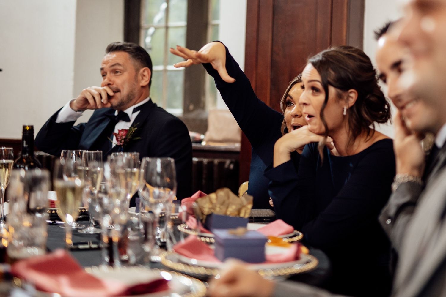 Wedding guests share animated conversations around elegant dining tables at a reception.