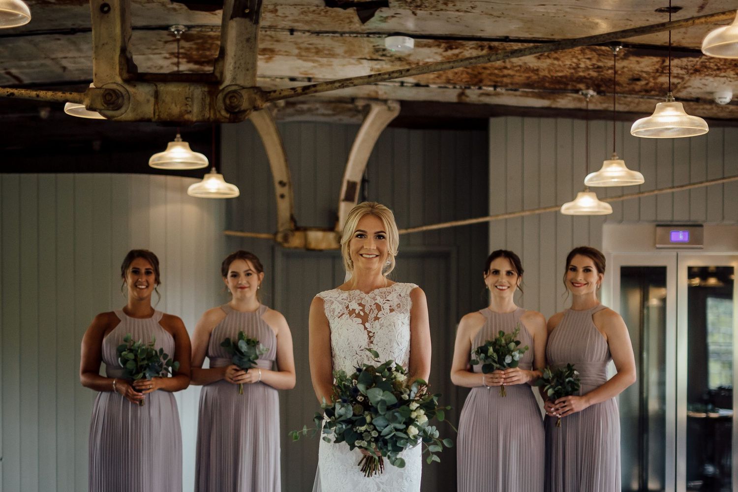 Wedding party gathered in rustic venue with industrial lighting fixtures.