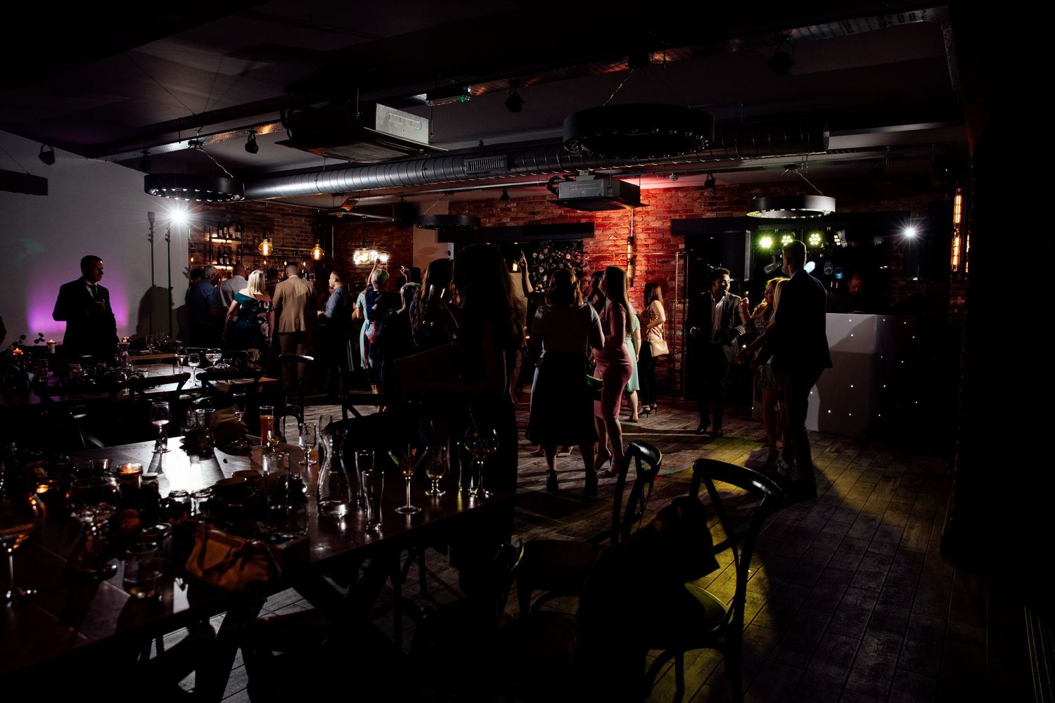 Dark and moody wedding reception venue with dramatic lighting and silhouetted guests.