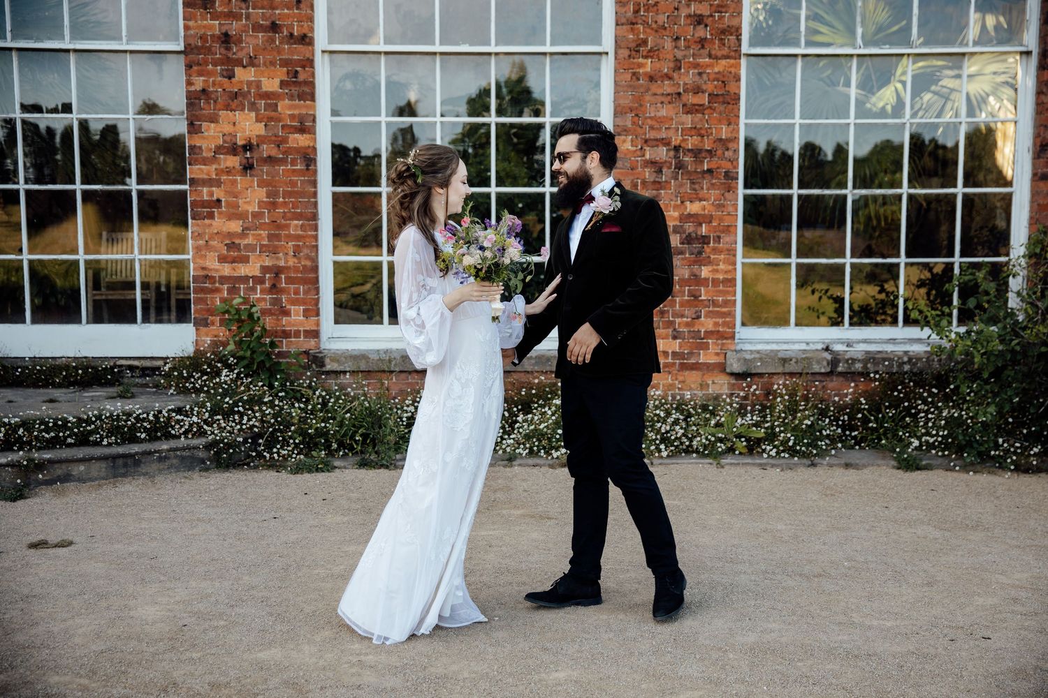 A couple dances together in front of a brick building with large windows during a wedding celebration.