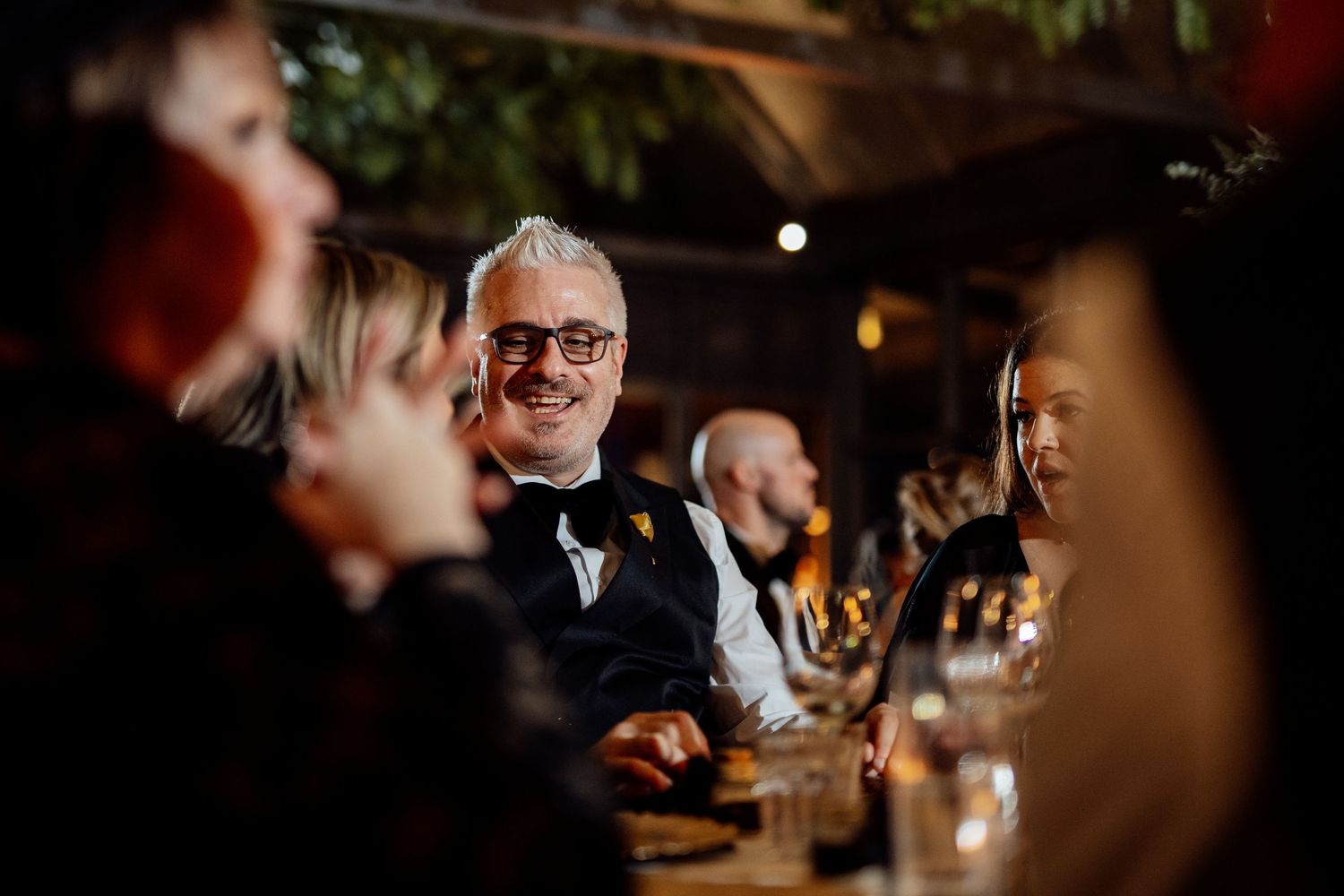 Wedding guests laughing and socializing during an intimate indoor reception dinner.