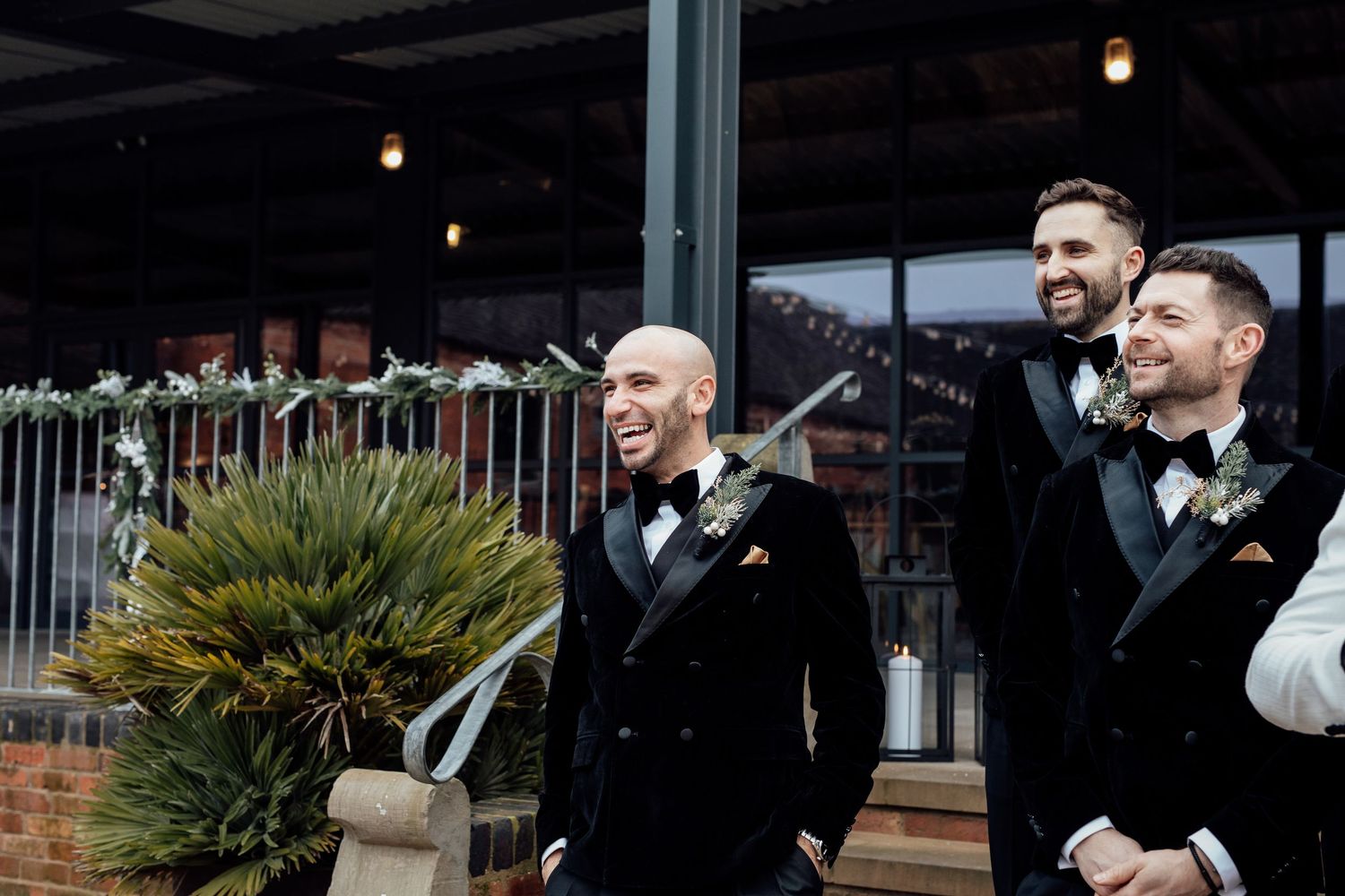 Wedding party members in black tuxedos gather under warm lighting at an elegant venue.
