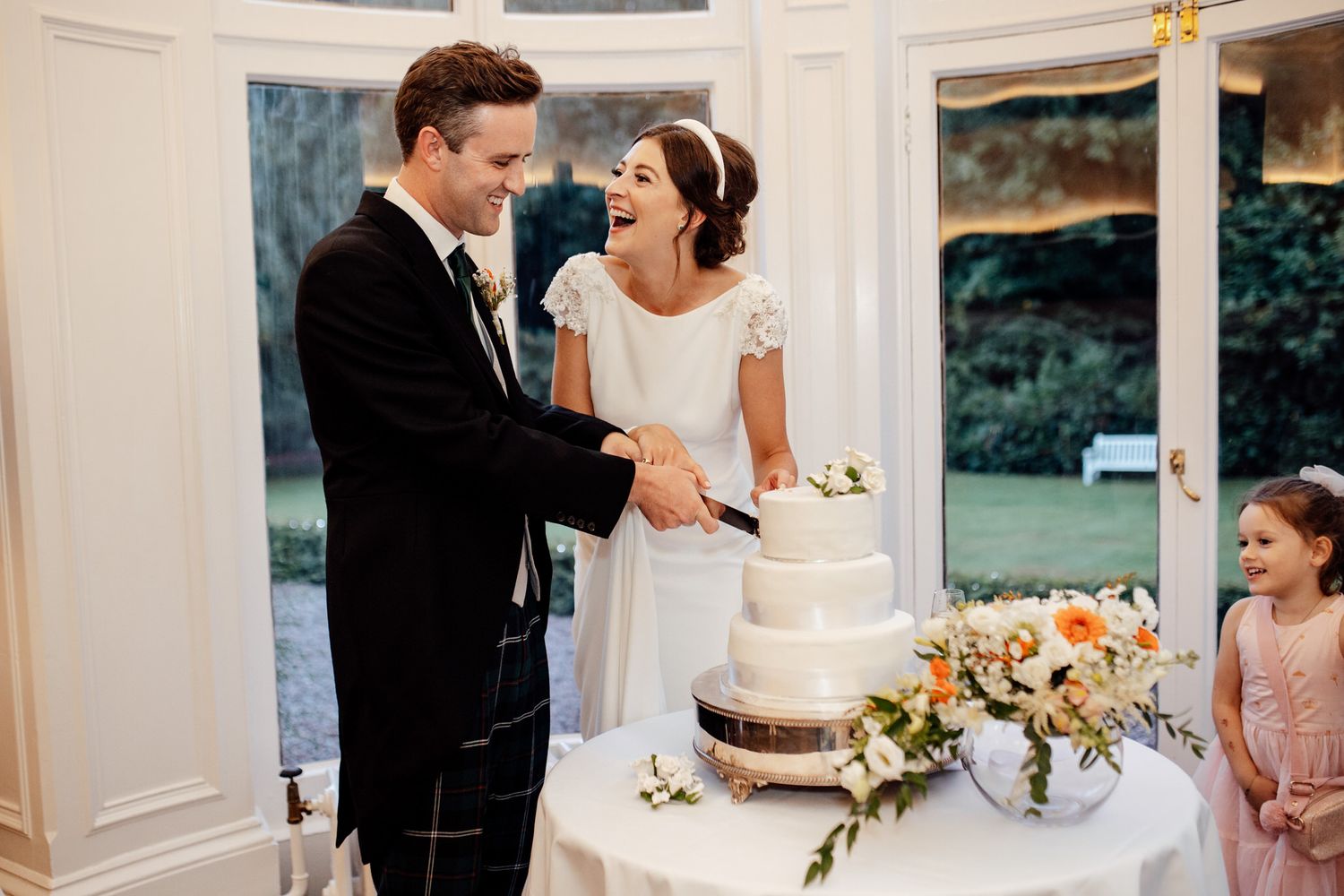 Elegant wedding reception setup with white decor and floral arrangements in a sunlit room.