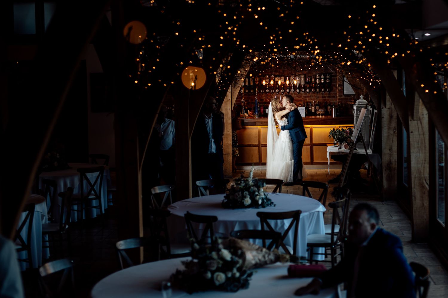 Romantic silhouette of couple dancing under twinkling lights at rustic barn reception.