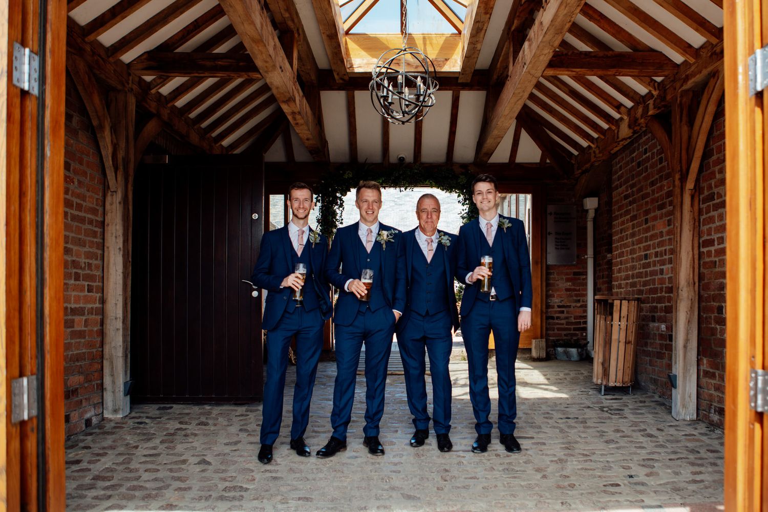 Wedding party in navy suits poses inside a rustic barn with exposed wooden beams.