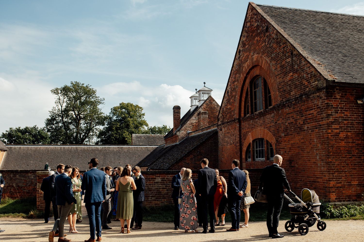 Exterior view of a historic red brick barn venue with guests gathering outside.
