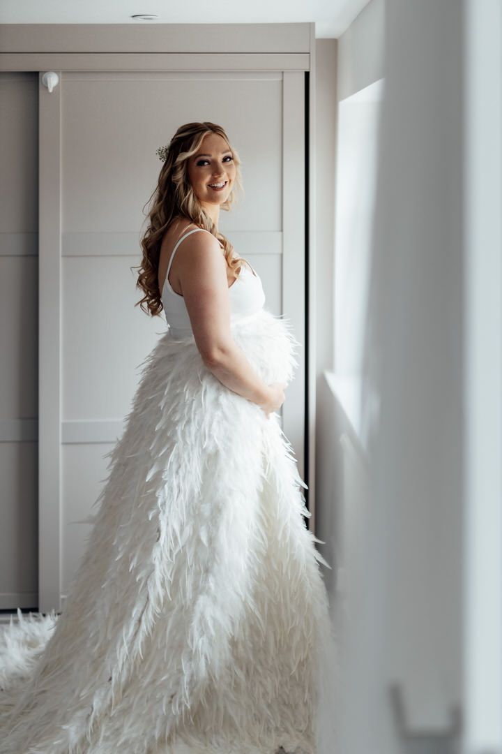 Elegant feathered wedding dress captured in a minimalist white hallway setting.