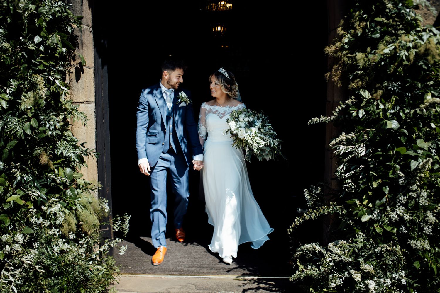 Couple poses against stone wall with greenery in outdoor wedding portraits.