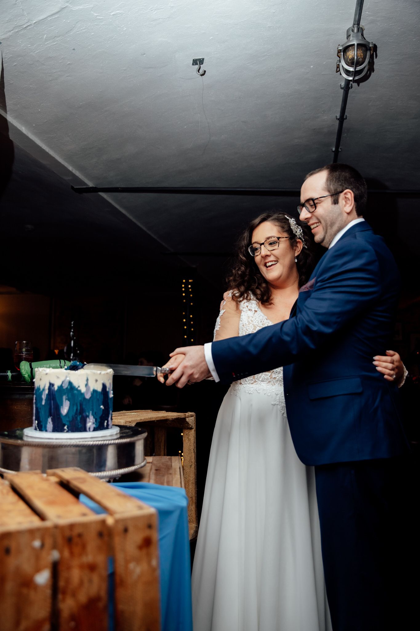 Couple cutting their blue and white wedding cake together at rustic venue.