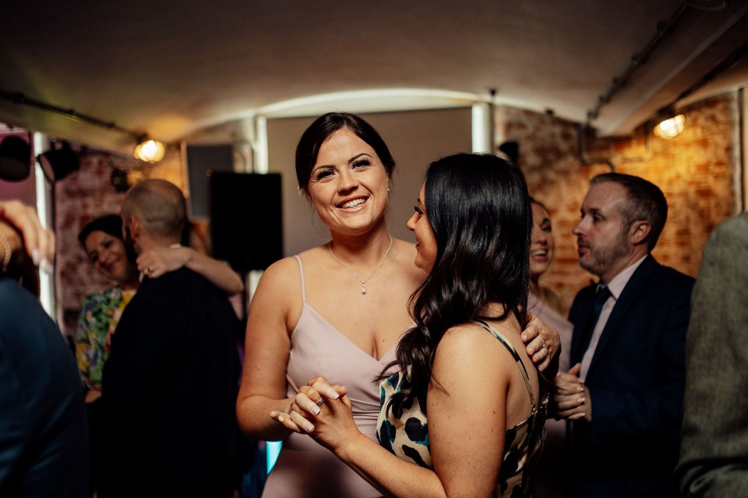 Wedding reception guests dancing and celebrating in a dimly lit venue.