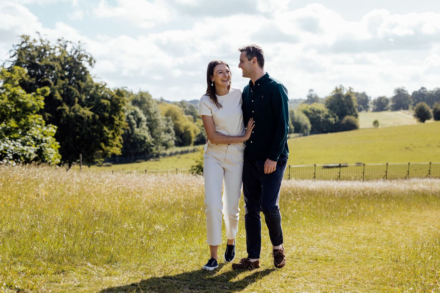 A couple enjoys a sunny afternoon in a rolling meadow with trees in the distance.