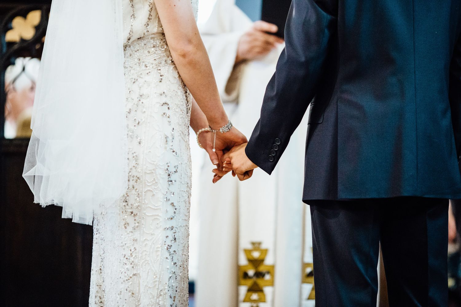 Wedding ceremony details showing white dress and dark suit in church setting.