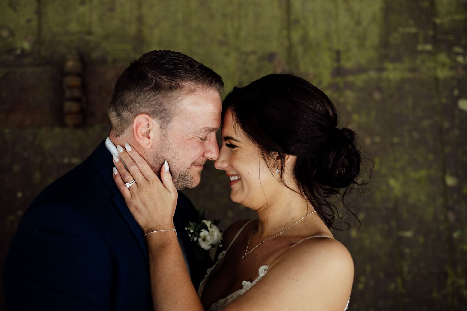 Romantic couple portrait against textured dark wall with dramatic lighting.