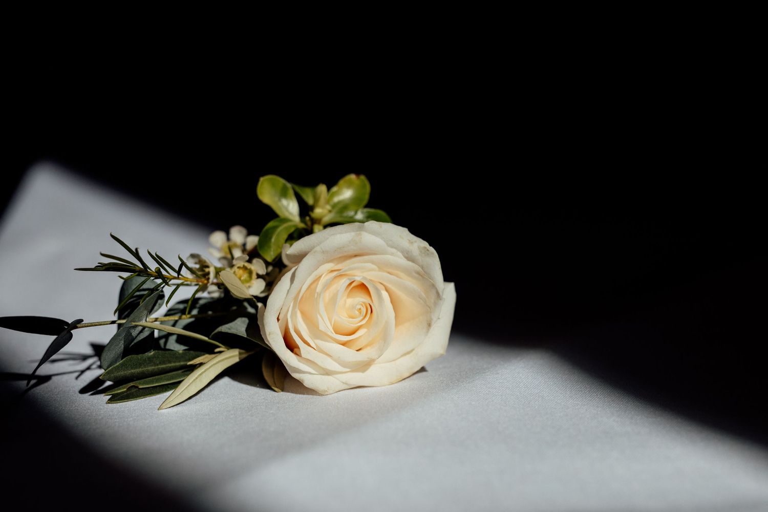 White roses and greenery arranged artistically against a dark background in a wedding detail shot.